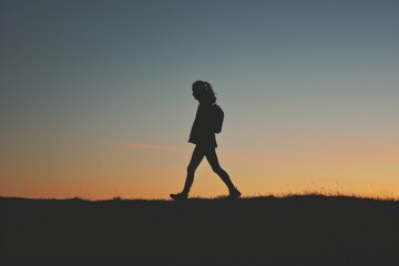 A lone figure traverses the rugged terrain, bathed in the golden glow of the setting sun, her silhouette a striking contrast against the vast expanse of the sky