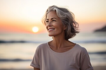 Portrait of a tender woman in her 50s dressed in a casual t-shirt against a vibrant beach sunset background. AI Generation