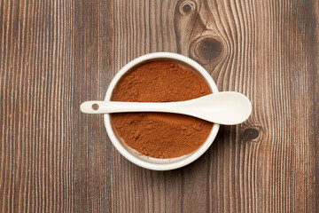 Cacao en polvo dentro de un cuenco blanco junto a una cuchara sobre un fondo de madera rústico. Vista superior y de cerca. Copy space