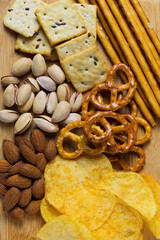 Assortment of crispy appetizers. Almonds, pistachios, Crackers, potato chips and mini pretzels. Wooden plate with Salty snacks on a white background. Party mix. top view. vertical