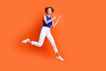 Fototapeta na wymiar Full length portrait of overjoyed person jumping indicate fingers empty space offer isolated on orange color background