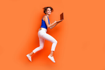 Fototapeta na wymiar Full length profile photo of attractive sportive person jump rush use netbook empty space isolated on orange color background