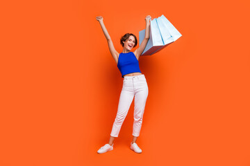 Full length photo of gorgeous overjoyed person hold raise store mall bags isolated on orange color background