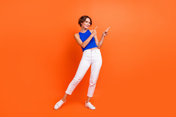 Full length photo of lovely positive person indicate fingers empty space proposition isolated on orange color background