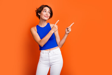 Photo of dreamy shiny girl dressed blue top showing two fingers looking empty space isolated orange color background