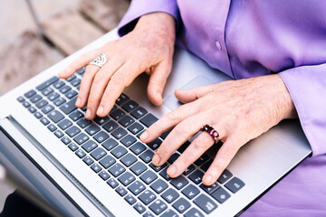 Fototapeta na wymiar close-up of the hands of a senior woman typing on the keyboard of a laptop, concept of technology and elderly people leisure