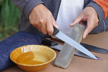 Closeup man hands sharpen knife on whetstone sharpener or grindstone. Concept, maintenance tools for cooking, make knife sharp ,not dull for long live using. Original style.     