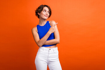 Photo of adorable dreamy lady wear blue singlet looking showing finger empty space isolated orange...