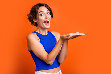 Photo of adorable excited girl dressed blue top open mouth holding arms empty space isolated orange color background