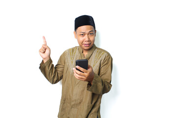 funny asian muslim man pointing to above with holding smartphone isolated on white background