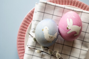 Easter serving. painted eggs with animal print bunny and bird, willow branches on textile napkin on plate.