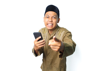 emotional asian muslim man pointing at camera with holding mobile phone isolated on white background