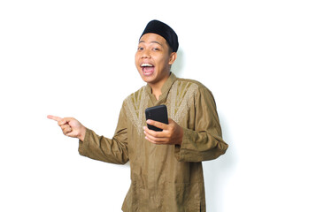funny asian muslim man screaming while pointing to beside with holding moblie phone isolated on...