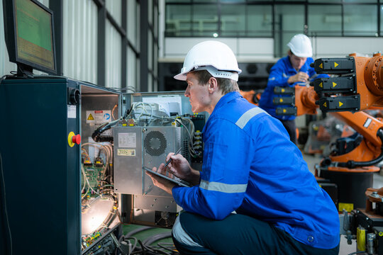 Technician working on the electrical control cabinet of robotic arm, Robotic arms industrial background - Powered by Adobe