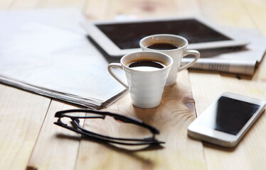 Black coffee with blank digital tablet and mobile phone, magazines and glasses on the table