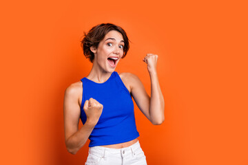 Photo of lucky excited girl dressed blue top rising fists shouting yes empty space isolated orange color background