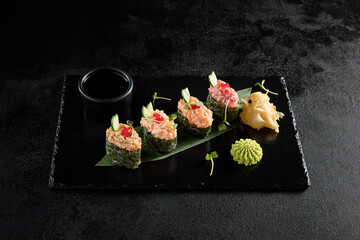Spicy sushi assortment gunkan style with salmon, shrimp, tuna, and eel on a black slate