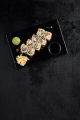 Top view of a Bonito roll with tuna flakes and salmon inside, served on a black slate with soy sauce, wasabi, and ginger