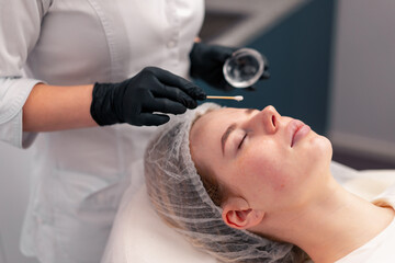 close-up doctor cosmetologist applies gel with a cotton swab on the face of a client procedure 
