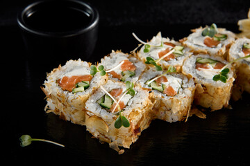 Bonito roll with tuna flakes and salmon inside, served on a black slate with soy sauce, wasabi, and ginger