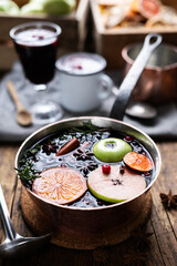 Mulled wine with slices of orange, apple, cinnamon, star anise, rosemary and cranberries in copper pot on kitchen table. Food photography