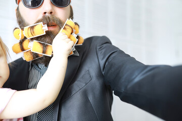 Baby infant hands grab beard of man.Cheerful hipster man with curlers in a beard.