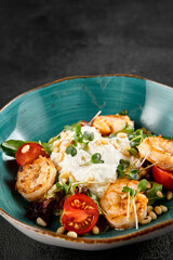 Salad with grilled shrimp and stracciatella cheese, accompanied by greens and cherry tomatoes in a turquoise bowl
