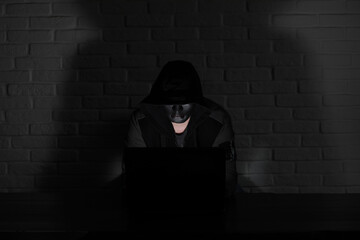 Hacker in black mask and hood at the table