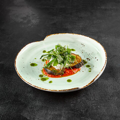 Baked eggplant with tomatoes and cheese, garnished with fresh greens on a ceramic plate
