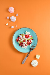 Artistic top view of pancakes with whipped cream and berries on a light blue plate, with an orange background