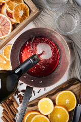 Making mulled wine in home kitchen. Red wine pouring into a copper pot. Slices of orange, cinnamon, star anise on table. Food photography