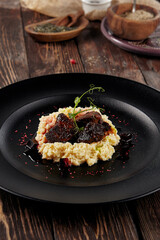 Braised beef cheeks with millet on a black plate, served on a rustic wooden table