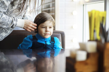 A young boy sits at a table near the window in a cafe and waits for a waiter to come up and take an...