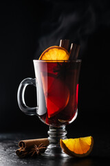 Hot mulled wine in a glass with slice of fresh orange and cinnamon sticks on a black background. Food and drink photography