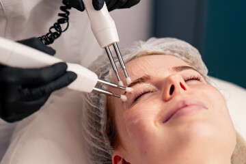 Fototapeta premium a close-up beautician conducts a microcurrent cosmetic procedure on a client's face in beauty salon
