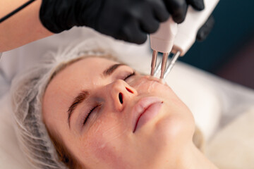 a close-up beautician conducts a microcurrent cosmetic procedure on a client's face in beauty salon
