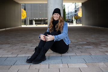 Red-haired woman with black jeans, black sweater and denim jacket in an urban location.