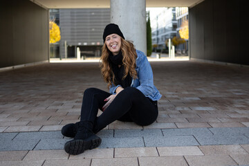 Red-haired woman with black jeans, black sweater and denim jacket in an urban location.