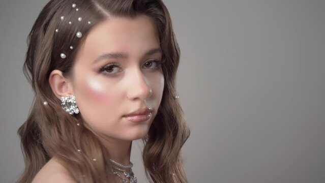 Portrait of a young beautiful female model with evening makeup, diamond necklace, ring, earrings and hairstyle Hollywood Wave, decorated with pearls, posing in the studio on a white background.