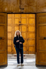 Palermo, Sicily, Italy A woman tourist stands inside the Carmine Maggiore Church and wooden doors.