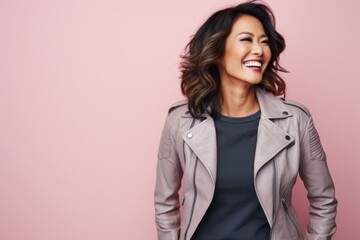 Portrait of a smiling asian woman in her 40s sporting a classic leather jacket against a pastel or...