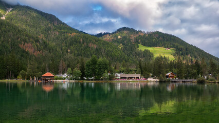 Fototapeta na wymiar Blick über einen See mit Gebäuden am gegenüberliegenden Ufer und einem Berghang mit Wald im Hintergrund
