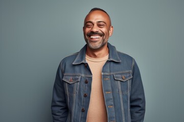 Portrait of a grinning indian man in his 40s sporting a rugged denim jacket against a pastel or...