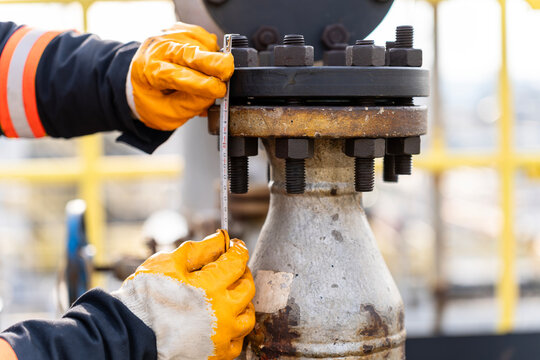 Male work hands wearing safety gloves taking measurements for replacement of studs and nuts on equipment flanges