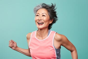 Portrait of a happy asian woman in her 50s wearing a lightweight running vest against a pastel or...