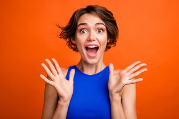 Photo of good mood impressed girl dressed blue top smiling open mouth rising arms isolated orange...