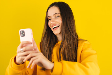Great application or website. Portrait of excited woman using her mobile phone, isolated on yellow...