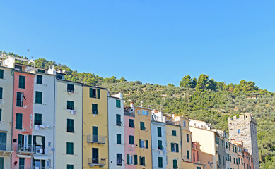Fototapeta na wymiar Typical colourful high and narrow houses with dark green shutters in Portovenere in the Gulf of the Poets at the Ligurian coast, Italy, with hill in the back and blue sky on a bright September day