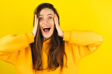 Optimistic woman reaction hands hold head wow, happy to receive awesome present from someone, shouts loudly, dressed in yellow hoody, isolated on yellow background. Excited female yells, happy scream.