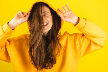 Close up photo of trendy cheerful cute nice sweet youngster laughing looking away toothy wearing hood isolated over yellow color background. Funny girl look playful holding hood. - obrazy, fototapety, plakaty